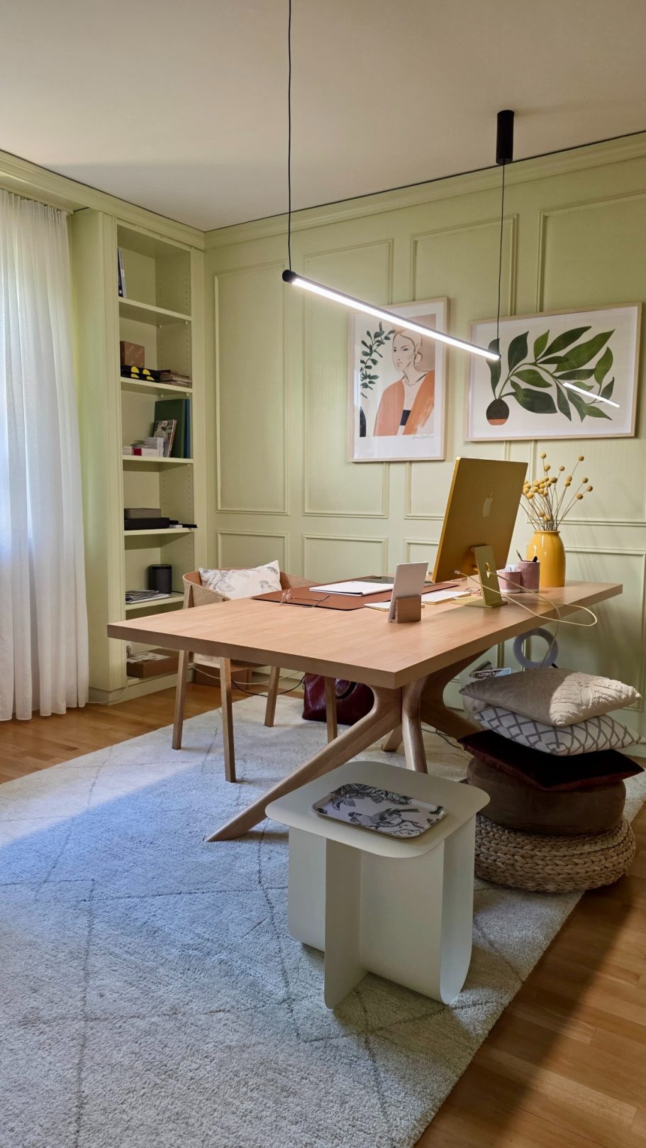Heller Arbeitsbereich mit grünem Wandfarben, Tisch, Stuhl und Regalen voller Bücher.