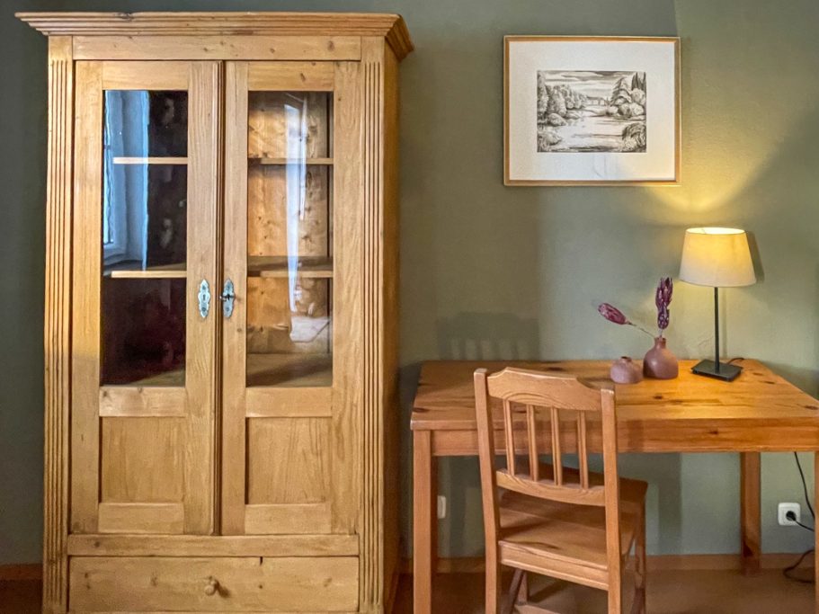Schlafzimmer mit Home Office Holzschrank, Holztisch, Stuhl und Tischlampe in einem gemütlichen Raum. Schlafzimmer mit Home Office einrichten BonTemps wohnen.