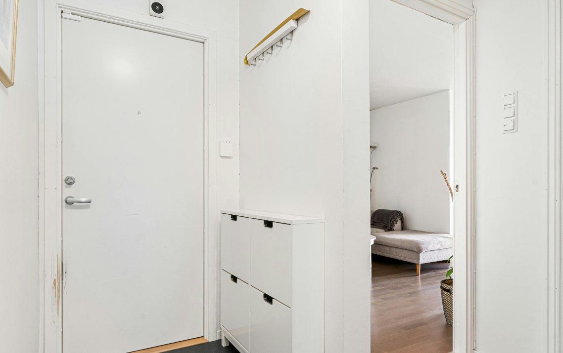 Weißer Flur mit Garderobe und Ablage, links eine Tür, rechts eine Couch.