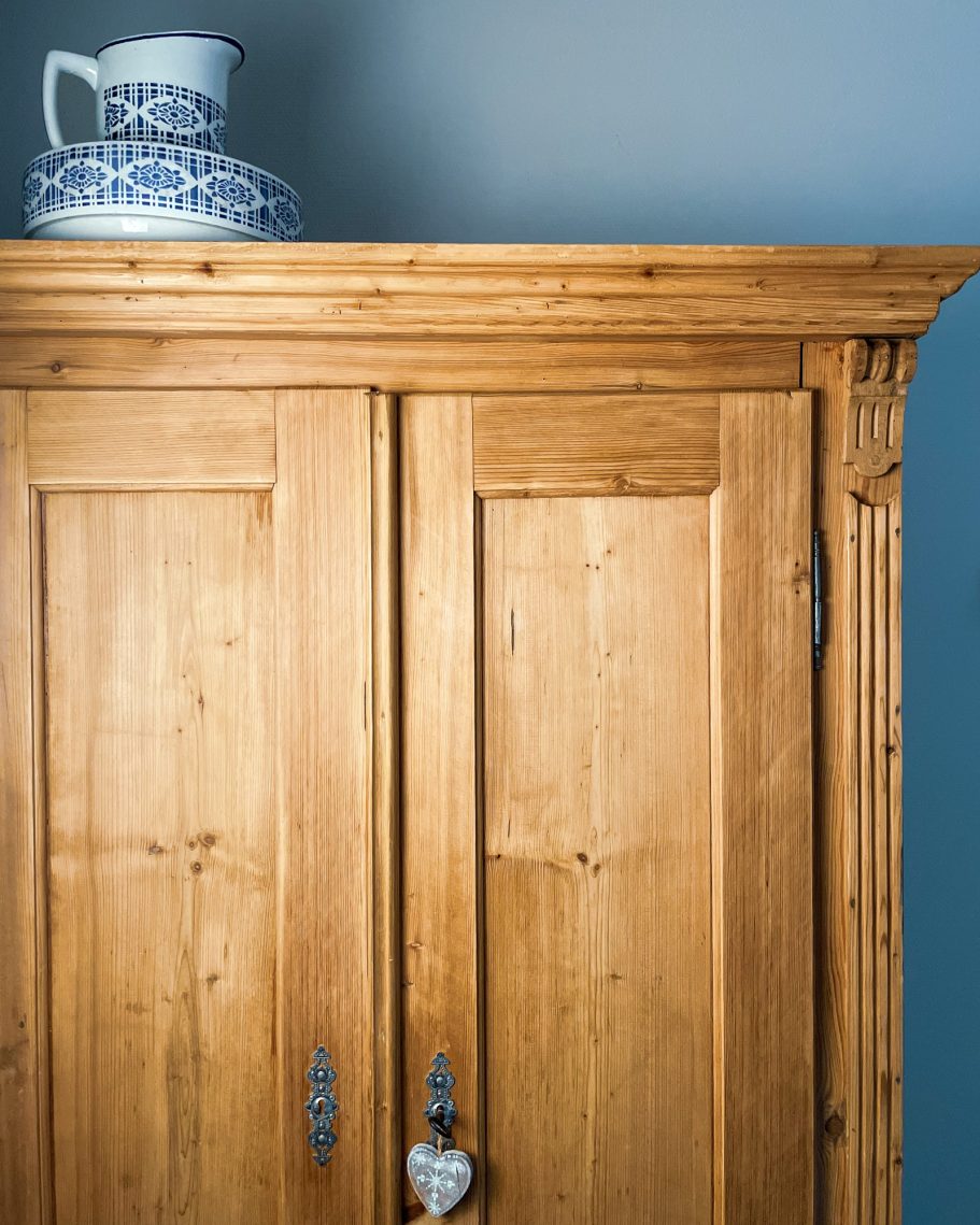 Holzschrank mit zwei Türen und einer blauen Keramikkaraffe oben drauf.