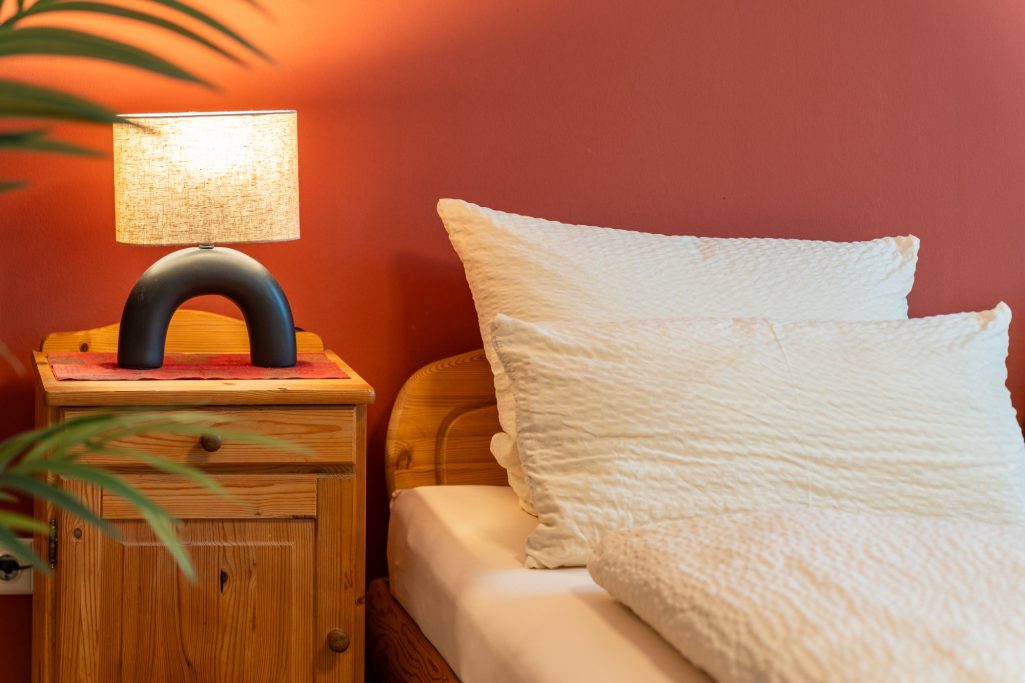 Schlafzimmer gemütlich einrichten Ein gemütliches Schlafzimmer mit einem Bett, Kissen und einer Tischlampe auf einem Nachttisch. Schlafzimmer einrichten BonTemps wohnen.