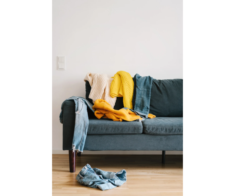 Grau-sofa mit verstreuten Kleidungsstücken in Gelb und Blau auf dem Boden.