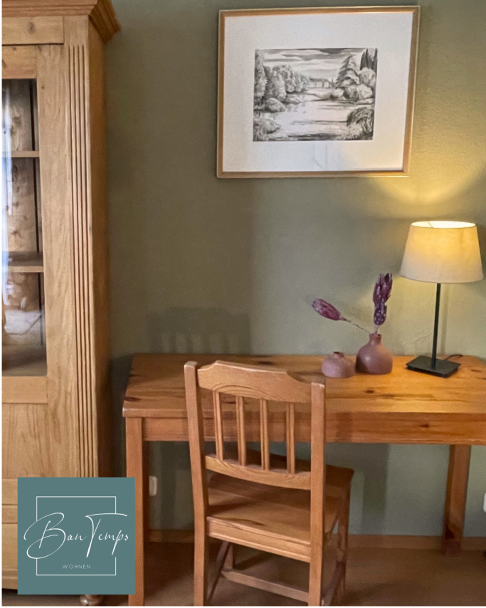 Holztisch mit einem Stuhl, Lampe und einer Blume in einer Vase an einer Wand.