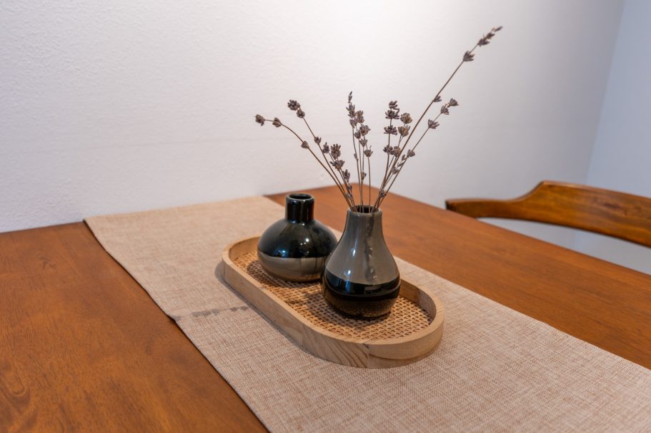 Zwei Vasen auf einem Tablett, eine mit Trockenblumen, auf einem Tisch mit Tischdecke.