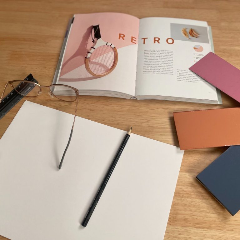 Offenes Buch mit Brille, Bleistift und Farbfächer auf einem Tisch.