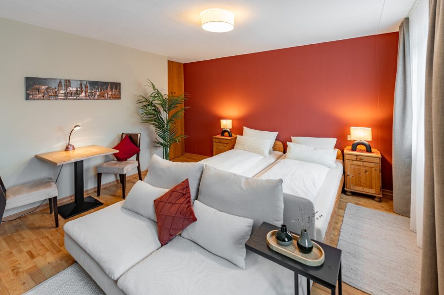 Modernes Schlafzimmer mit zwei Einzelbetten, gemütlicher Sitzecke und Schreibtisch.