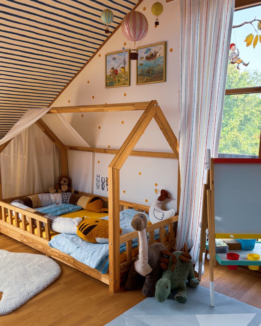 Ein helles Kinderzimmer mit einem Holzhausbett, bunten Dekorationen und Spielzeug.