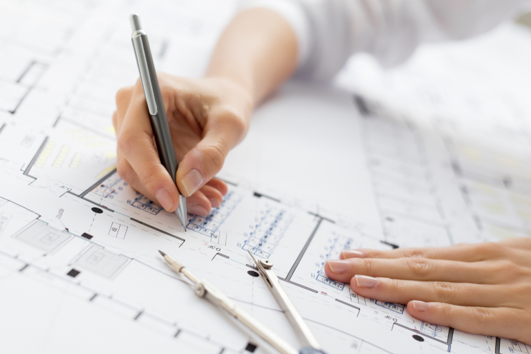 Hand, die mit einem Stift auf einem Architekturplan arbeitet, mit Lineal und Schablonen.