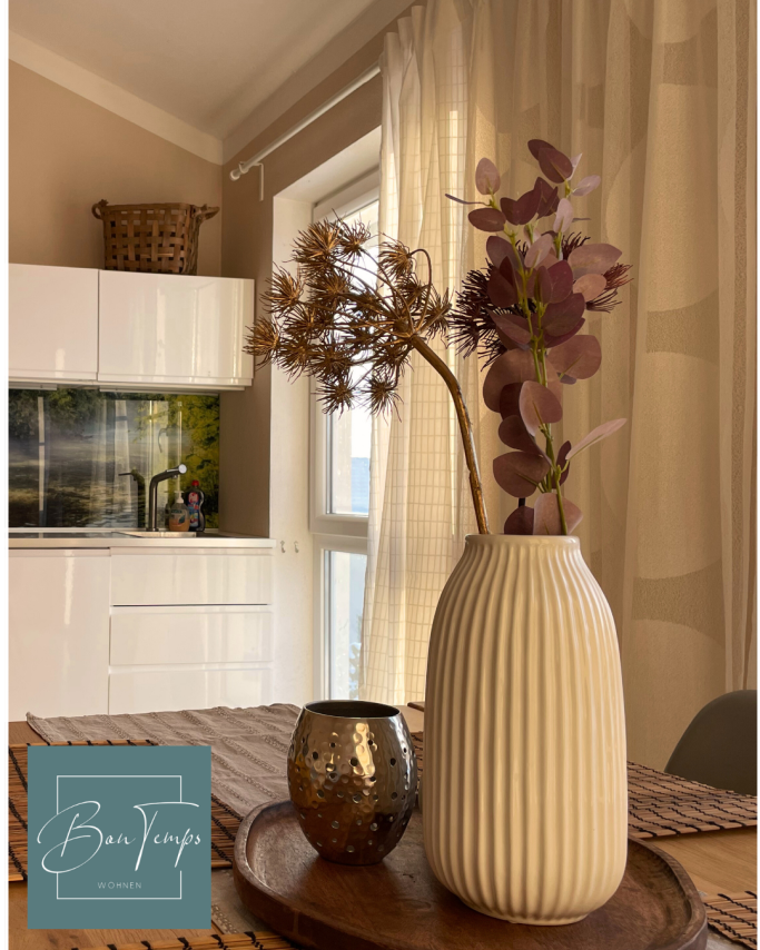 Moderner Raum mit einer weißen Vase, Trockenblumen und einer dekorativen Schale.