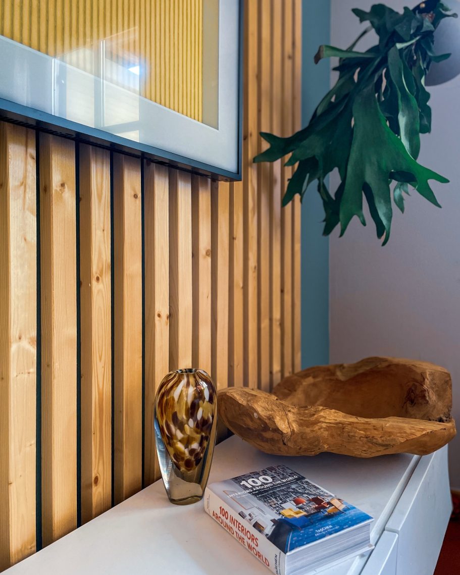 Eine dekorative Vase und eine Holzschale auf einer weißen Oberfläche, gefasst von Wandplatten.