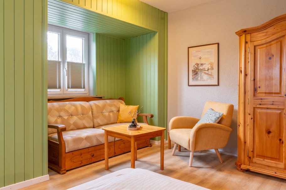 Wohnzimmer mit einer Holzcouch, einem Sessel, einem Tisch und einer grünen Wand.