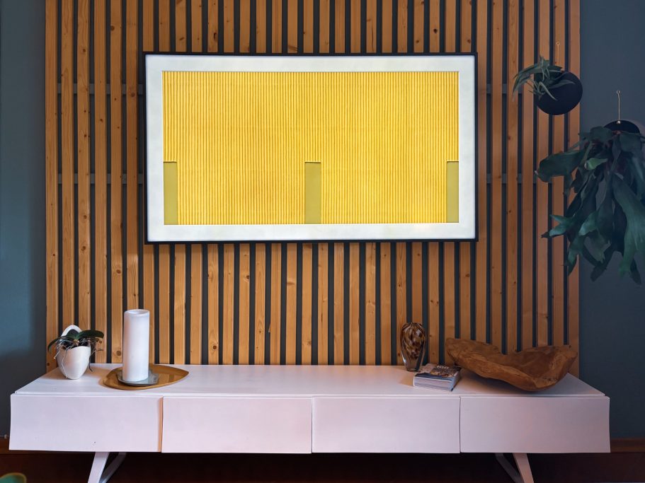 Moderne Wohnwand mit gelbem Gemälde, Pflanzen und minimalistischer Möbelstück.
