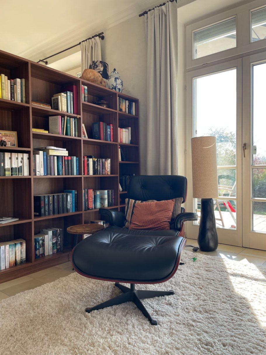 Schwarzer Sessel mit Ottoman, Bücherregal im Hintergrund, Fenster mit Tageslicht.